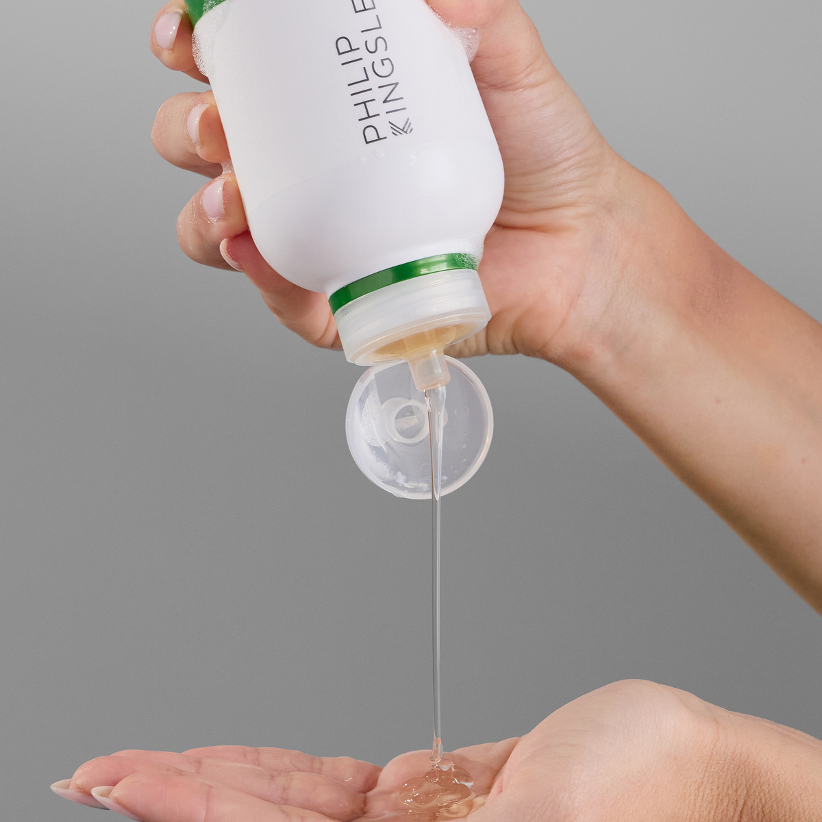 Das Shampoo gegen schuppige, juckende Kopfhaut von Philip Kingsley aus einer weißen Flasche mit grünem Verschluss in die offene Handfläche geben.