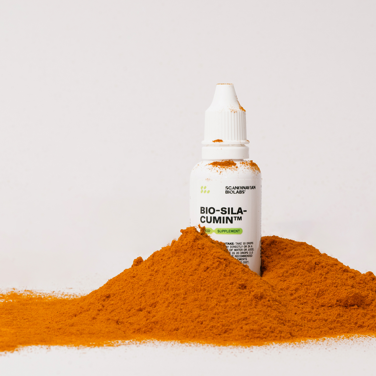 Eine weiße Flasche mit Bio-Silacumin von Scandinavian Biolabs steht auf einer weißen Fläche, umgeben von einem Haufen orangefarbenem Kurkumapulver.