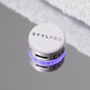 Das STYLPRO LED Spot & Blemish Patch, ein weißes, rundes Gerät mit blauem Licht, wird auf einer reflektierenden Oberfläche neben einem weißen Handtuch angebracht.