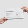 Zwei Hände halten eine weiße Schachtel mit der Aufschrift Kopfkissenbezug von Transparent Lab vor einem schlichten Hintergrund.