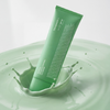 Eine Tube „Transparent Lab Mineral Redness Control CC Cream“ spritzt in eine grüne Flüssigkeit, wobei um sie herum kleine Tröpfchen zerplatzen.