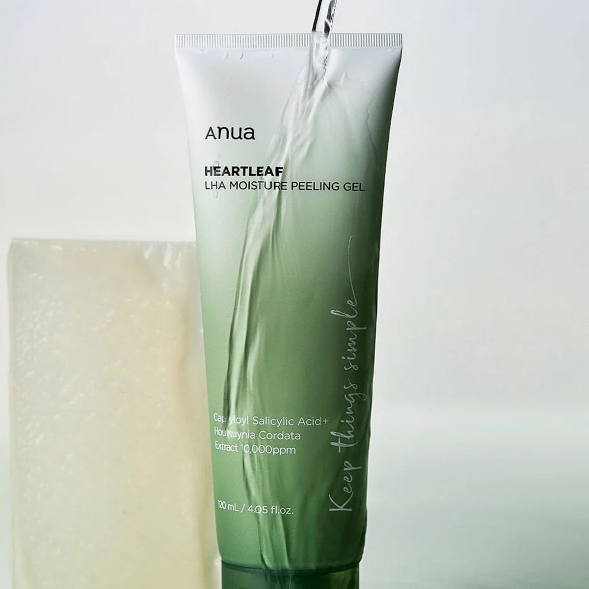 Eine Tube Heartleaf LHA Moisture Peeling Gel, über die Wasser gegossen wird, neben einem weißen rechteckigen Block.