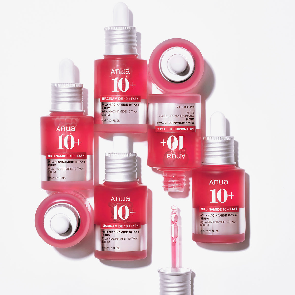 Sieben rosa Flaschen Niacinamide 10 % + TXA 4 % Dark Spot Correcting Serum, angeordnet auf einem weißen Hintergrund, bei einigen sind Tropfer sichtbar.