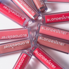 Neun Tuben „BLONDESISTER 2 IN 1 SWEET GLOSS TINTED LIP OIL“ in verschiedenen Farbtönen, kreisförmig auf einer weißen Fläche angeordnet.