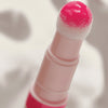 Nahaufnahme eines Applikators mit glänzendem pinkem Lip Oil, die Spitze ist flauschig und mit Farbe benetzt.
