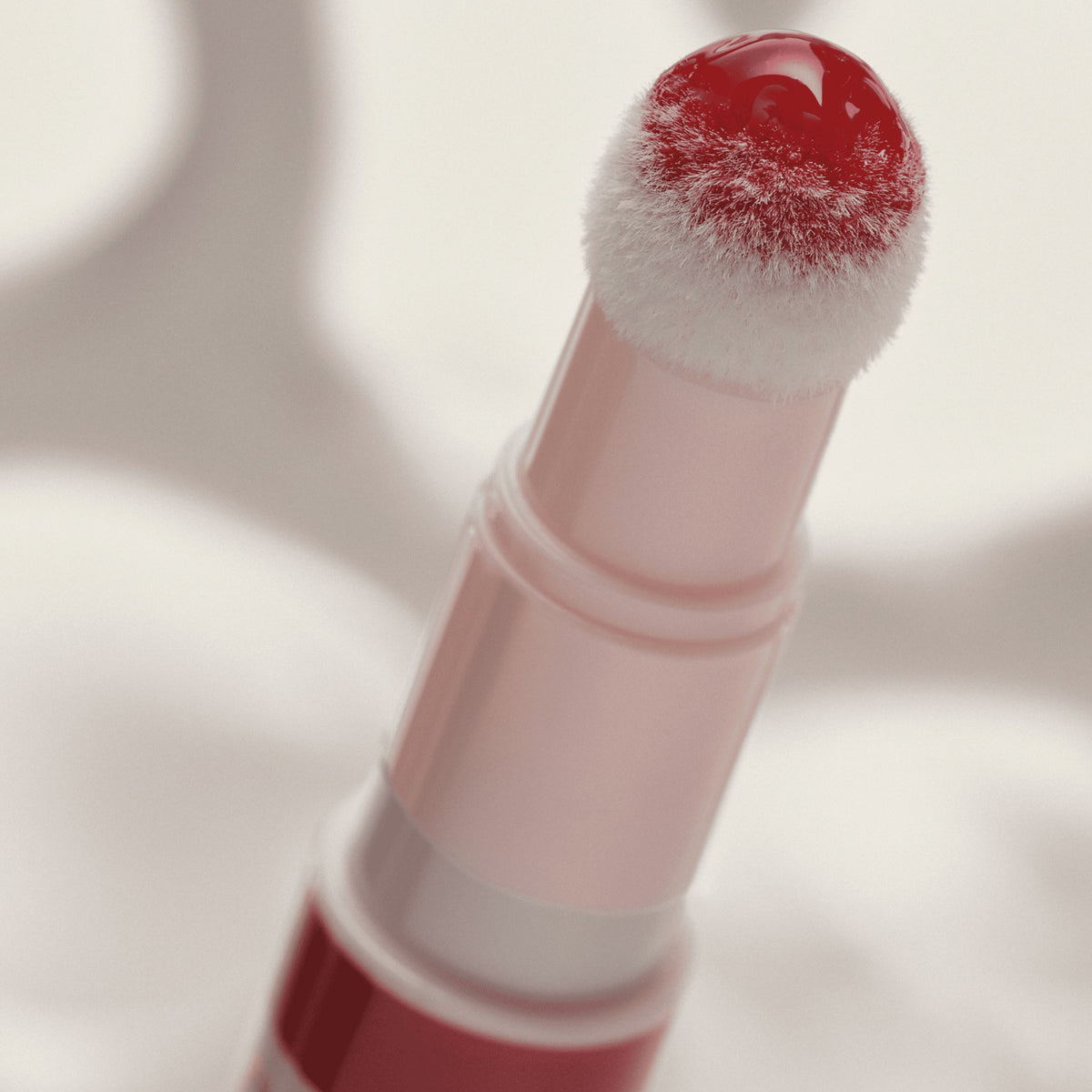 Nahaufnahme eines Applikators mit rotem, glänzendem Catrice Colour Cushion Lip Oil, das auf der weißen, flauschigen Spitze schimmert.