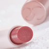 Nahaufnahme des Catrice Diamond Glaze Gloss Stick in einem schimmernden Rosaton, liegend mit sichtbarer Produktspitze und glänzendem Deckel im Hintergrund.