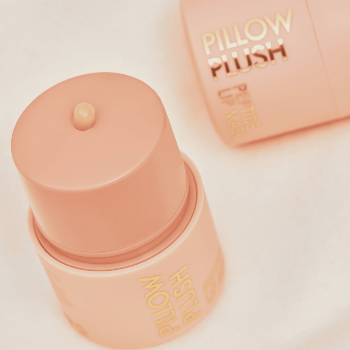 Die Pillow Plush Peptide Lip Mask 010 von Catrice Cosmetics in pfirsichfarbenen Behältern auf einem weichen, hellen Hintergrund.
