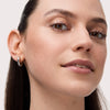 Eine Frau mit glatter Haut, natürlichem Make-up und silbernen Ohrringen lächelt leicht in die Kamera und präsentiert ihre voluminösen Wimpern.