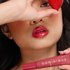 Frau hält eine Erdbeere in der Nähe ihres Auges, trägt glänzendes Make-up und Juicy Lip Balm von Dominique Cosmetics auf ihren Lippen.