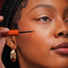 Eine Frau trägt falsche Sommersprossen mit Freck Noir von Freck Beauty auf ihre Wangen auf und trägt goldene Ohrringe.