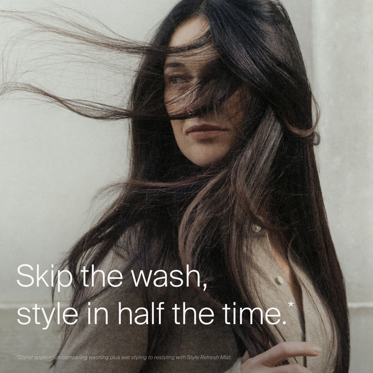 Frau mit langem, dunklem Haar im Wind: Erfrischen Sie Ihr Haar schnell mit Living Proof Perfect Hair Day Style Refresh Hair Mist.