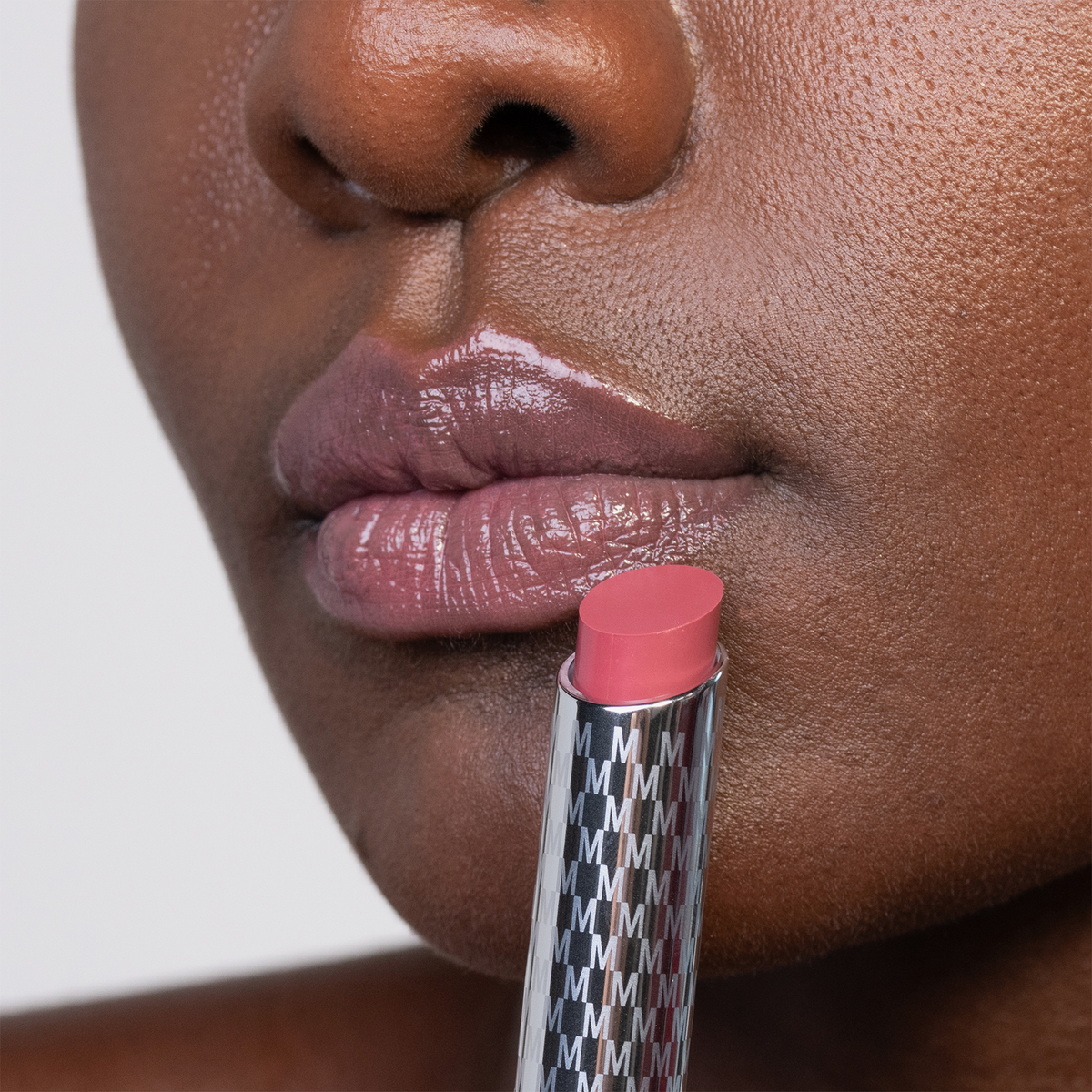 Nahaufnahme von glänzenden Lippen und dem rosa Lippenstift THE HYDRAMORPHOSIS TWIN SET von Mesauda Beauty in einer Metalltube, der in der Nähe des Mundes gehalten wird.