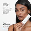 Eine Frau hält Minimalist Light Fluid SPF 50 Sunscreen neben ihrem Gesicht; der Text hebt die UV-Filter und den hohen Sonnenschutz hervor.