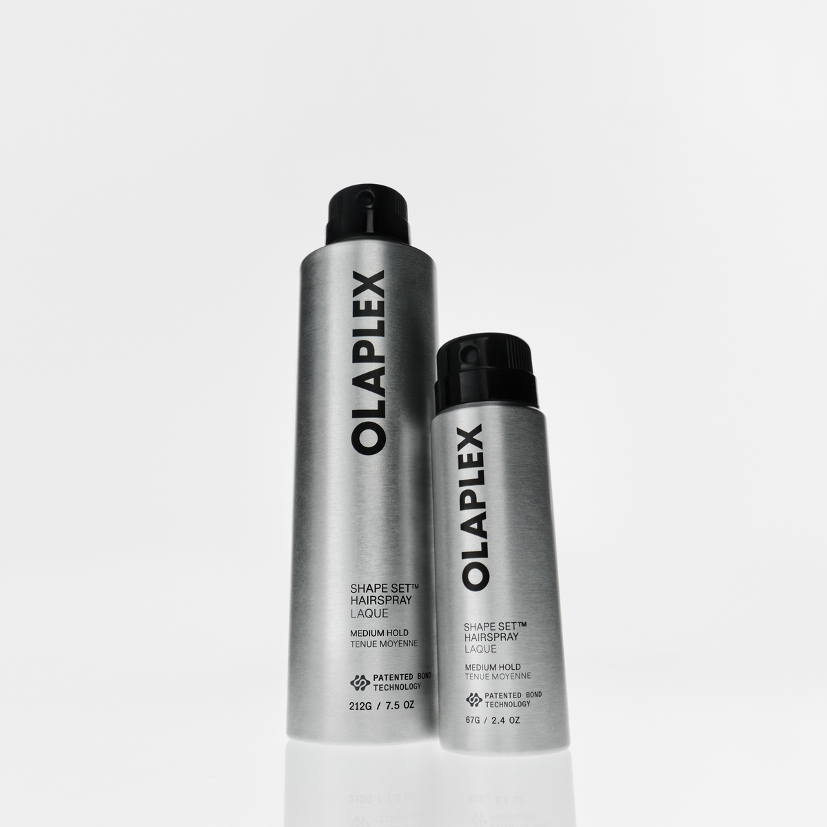 Zwei silberne OLAPLEX Shape Set Haarspray-Sprühdosen unterschiedlicher Größe mit schwarzen Sprühköpfen.