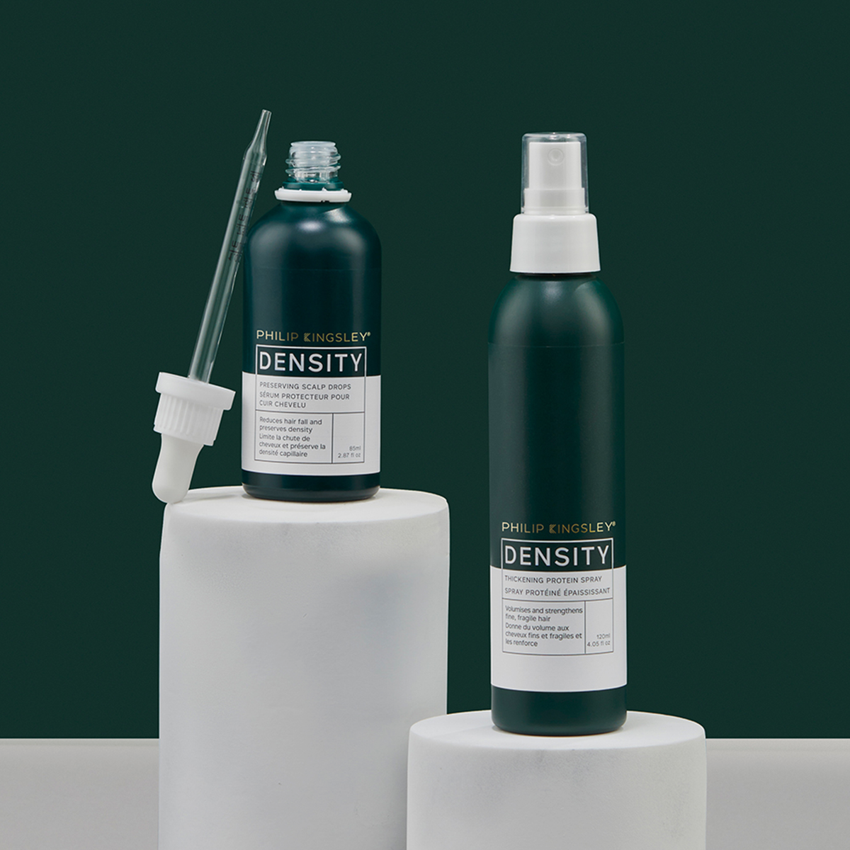 Philip Kingsley „Density Preserving Scalp Drops“ mit Tropfer und Sprühflasche auf weißen Sockeln, vor einem dunkelgrünen Hintergrund.