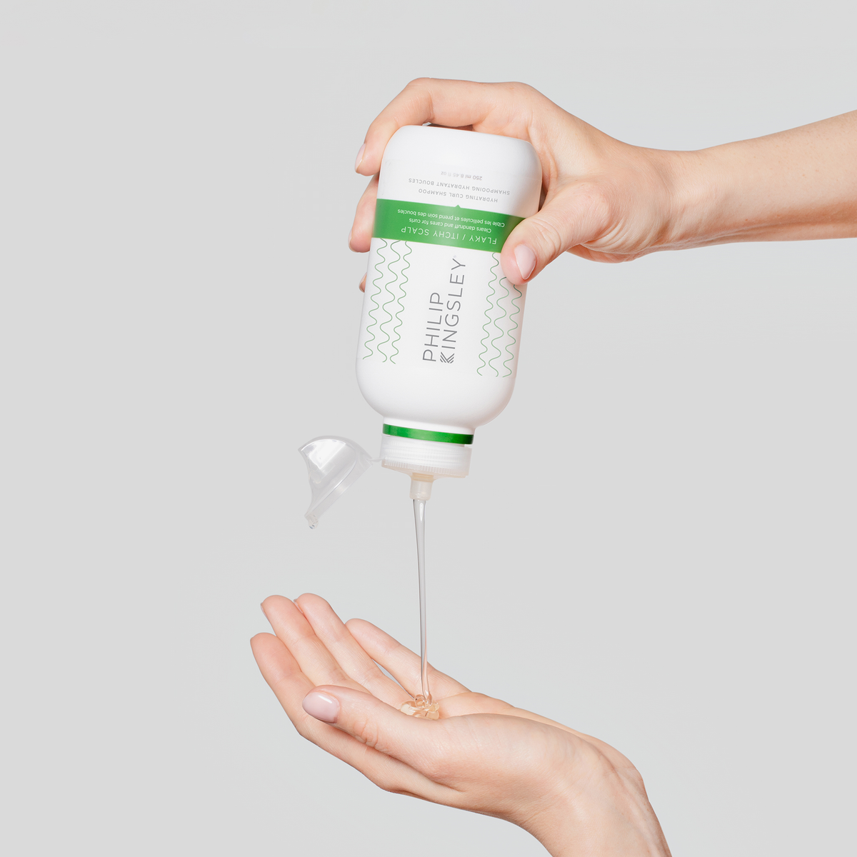 Vor einem schlichten Hintergrund gießt eine Hand das „Philip Kingsley Flaky/Itchy Scalp Hydrating Curl Anti-Dandruff Shampoo“ in eine offene Handfläche.
