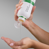 Vor einem grauen Hintergrund gießt jemand das „Philip Kingsley Flaky Itchy Scalp Shampoo“ aus einer weißen Flasche in seine Hand.