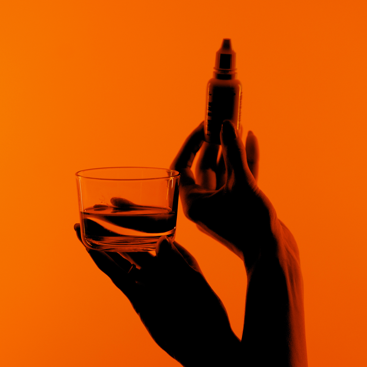 Hände halten ein Glas Wasser und eine Bio-Silacumin-Tropfflasche von Scandinavian Biolabs vor einem orangefarbenen Hintergrund.