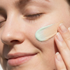 Mit geschlossenen Augen trägt eine Person sanft die „Transparent Lab Mineral Redness Control CC Cream“ auf ihre Wange auf und lächelt dabei sanft.