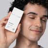 Eine Person mit lockigem Haar lächelt und hält die „Transparent Lab Mineral Sunscreen SPF 50“ neben ihr Gesicht.