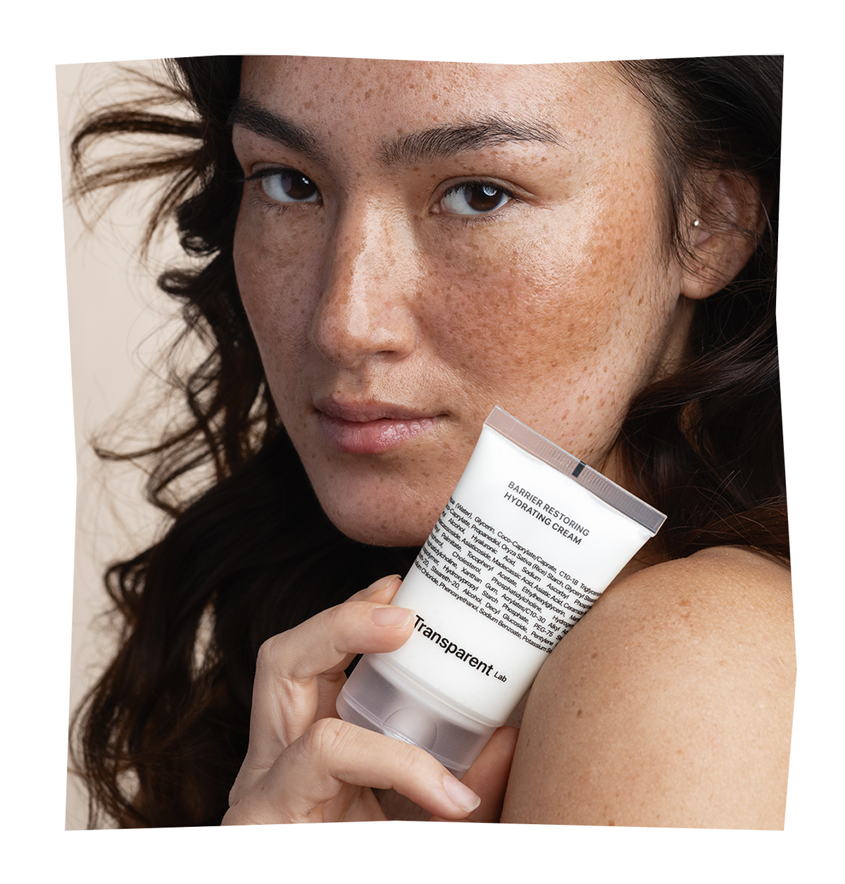 Eine Person mit Sommersprossen hält eine Tube „Transparent Lab Barrier Restoring Hydrating Cream“ an ihre Schulter.