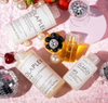 Olaplex-Haarprodukte mit Discokugeln, Früchten und Perlen auf einem rosa Samthintergrund.
