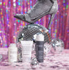 Drei Hautpflegeprodukte und eine Discokugel mit einem glitzernden Stöckelschuh vor einem glitzernden, bunten Hintergrund.