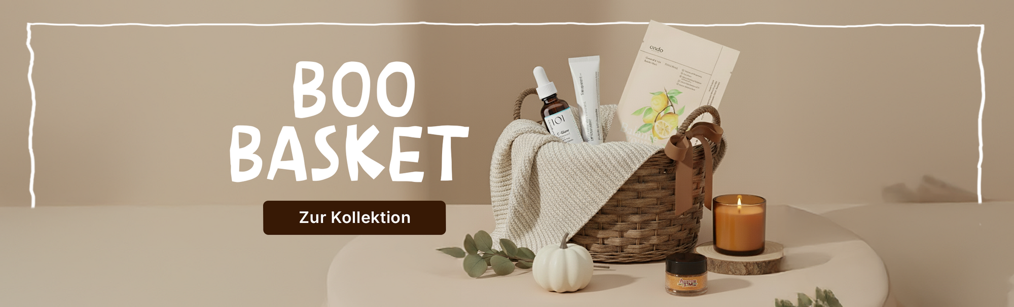 Gefüllter Korb mit Beautyprodukten, Decke, Kerze und Kürbis vor beigem Hintergrund, Text 'Boo Basket'.