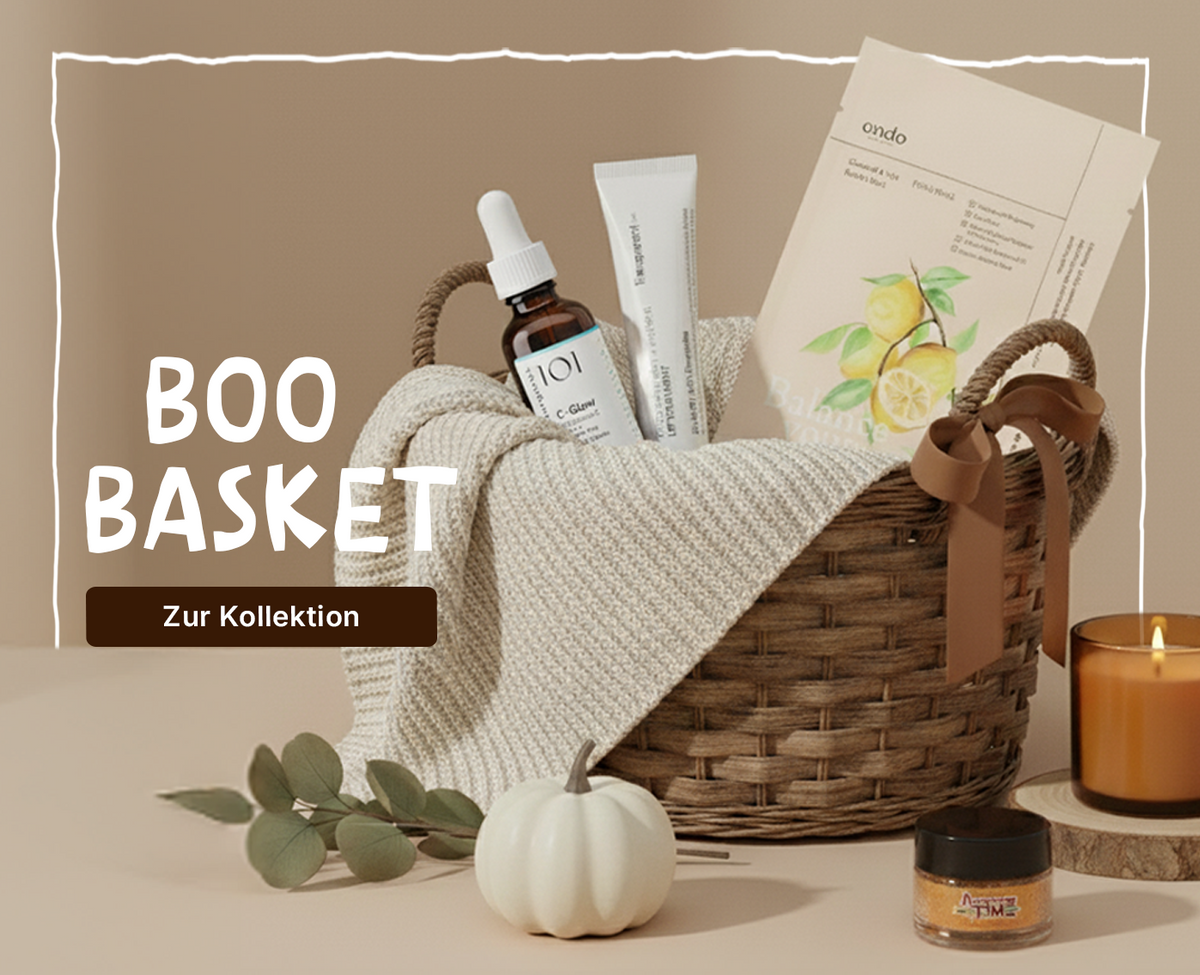 Gefüllter Korb mit Beautyprodukten, Decke, Kerze und Kürbis vor beigem Hintergrund, Text 'Boo Basket'.