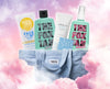 Eine hellblaue Purish-Tasche gefüllt mit Hautpflegeprodukten von Bondi Sands, The Fox Tan und SKIN1004, vor rosa Wolkenhintergrund.