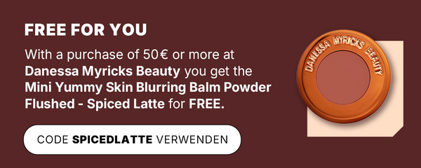 Advertising graphic with dark red background: Text about free promotion for purchases of €50 or more at Danessa Myricks Beauty. The image shows the Mini Yummy Skin Blurring Balm Powder Flushed in the colour Spiced Latte, in round packaging with a copper-coloured rim.