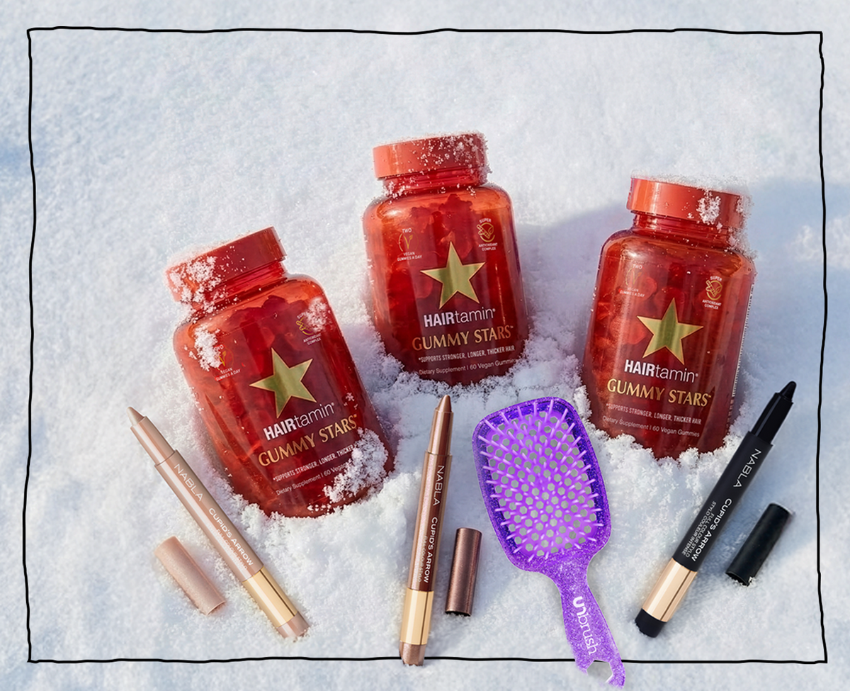 Drei HAIRtamin Gummy Stars im Schnee, umgeben von NABLA Cupid’s Arrow Stiften und einer lilafarbenen UNBrush-Haarbürste.