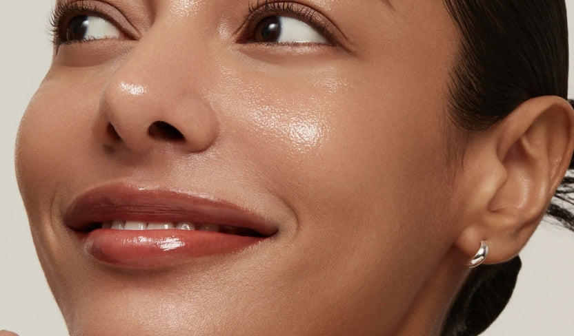 Nahaufnahme eines Gesichts mit strahlender Haut und dezent glänzenden Lippen, Blick leicht zur Seite gerichtet.